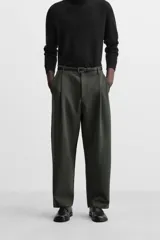 Pantalón relaxed fit color verde oscuro, con pliegues en la parte delantera, bolsillos laterales y traseros de ojal. Cierre frontal con cremallera y botón.