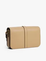Cartera de hombro color beige de acabado liso, con solapa frontal que se cierra con un broche metálico dorado con el monograma TH. Posee correa ajustable para llevar al hombro o cruzada.