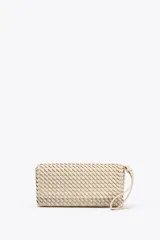 Bolso alargado color beige con diseño trenzado, asa bandolera y tirador con pulsera de mano. Incluye bolsillo interior y cierre con solapa y botón imantado.