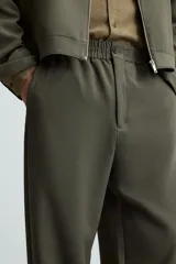 Pantalón verde oscuro de corte recto, con cintura elástica, bolsillos laterales y un bolsillo trasero. Cierre frontal con cremallera y botón.