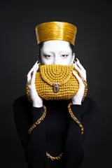 Cartera de mano tejida color dorado, con cierre metálico y cadena gruesa dorada.