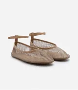 Zapatilla tipo bailarina color beige, con capellada de red calada, puntera redonda y tira de charol con hebilla en el tobillo.