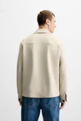 Sobrecamisa color beige de corte recto, con cuello solapa, manga larga con puños abotonados, cierre frontal abotonado, bolsillos de parche con solapa en el pecho y bolsillos de ojal en la cadera.