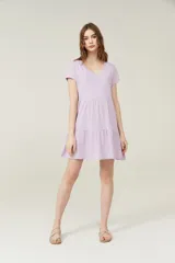 Vestido corto lila con cuello en V y mangas cortas. Tiene corte holgado y dos volados en la falda.