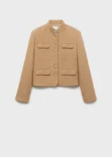 Chaqueta corta color beige de tweed con cuello mao, cierre frontal con botones y cuatro bolsillos delanteros con solapa.