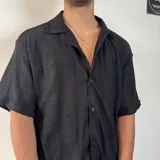 Camisa negra tejida con cuello solapa, manga corta y corte oversize.