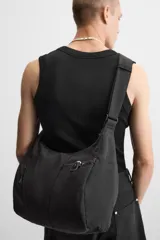 Bolso negro de tela técnica con correa de hombro ajustable. Tiene un compartimento principal con cierre de cremallera, un bolsillo interior con cremallera y tres bolsillos exteriores, uno de ellos con cremallera.