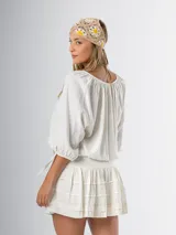 Blusa color crudo de algodón suave, con mangas 3/4 abullonadas con ajuste de cinta, botones frontales en el escote y elástico flojo en la cintura.