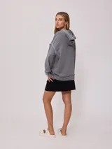 Canguro gris con capucha corta, bolsillo tipo canguro y parche con logo de la marca Rusty en el pecho. Tiene efecto lavado y costuras a la vista.