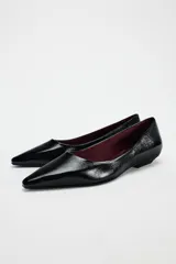 Zapato plano de charol negro con punta fina y suela baja.