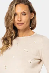 Buzo color beige de tejido de punto con bordado de pequeñas flores blancas.