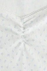 Remera corta blanca de punto suave con estampado de flores pequeñas. Modelo ajustado con costura fruncida en el centro del busto y escote corazón pronunciado con ribete de picot.