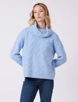 Buzo de punto grueso color celeste, con textura en relieve y cuello volcado. Tiene mangas largas de corte hombro caído y puños anchos en rib. El ruedo es recto con borde en rib.