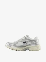 Zapatillas New Balance modelo 725, color blanco con detalles plateados y logo "N" en negro. Diseño inspirado en el estilo de carrera de los años 2000, con malla transpirable, entresuela con amortiguación y suela con agarre.