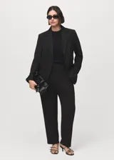 Blazer negro de diseño entallado, con solapas de muesca, hombros estructurados y cierre frontal de un solo botón. Presenta dos bolsillos de ribete delanteros y un bolsillo de ribete en el pecho.