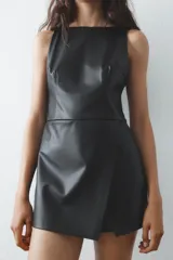 Mono corto negro de efecto piel, con cuello redondo y sisa. Presenta un corte cruzado en el delantero, costuras marcadas y cierre trasero con cremallera.