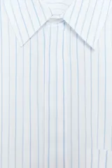 Camisa blanca corta con rayas verticales celestes, cuello solapa y mangas cortas con dobladillo. Tiene un bolsillo de parche en el pecho y cierre frontal con botones ocultos.