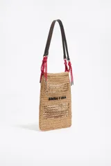 Bolso tote de rafia color beige con diseño calado, asas cortas de cuero marrón y cordones rojos decorativos.
