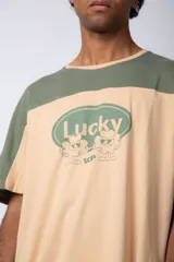 Remera color beige con mangas y parte superior en verde militar. Estampado frontal con texto "Lucky" y diseño de flores con rostro.