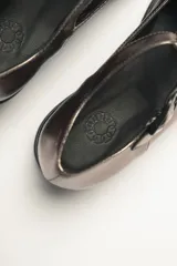 Zapato guillermina color bronce con acabado metalizado, con correa sobre el empeine con hebilla ajustable y suela de goma negra con plataforma.