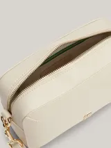 Cartera rectangular tipo bandolera de color blanco roto, con acabado liso y herrajes dorados. Presenta un monograma metálico TH en el centro y una correa ancha ajustable y extraíble.