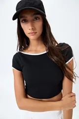 Top corto negro de punto acanalado con escote redondo, mangas cortas y ribetes blancos en cuello y mangas.