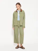 Chaqueta verde militar de algodón con cuello marrón de pana, cierre frontal con botones dorados, bolsillos plaqué en la parte superior e inferior y corte holgado.