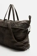Bolso de viaje marrón oscuro fabricado en piel con acabado craquelado. Tiene un compartimento principal con cierre de cremallera, un bolsillo plano interior con cremallera y dos bolsillos frontales con botón a presión. Cuenta con asas de mano de piel y asa de hombro removible y ajustable.