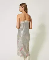 Vestido midi plateado de tirantes finos, cubierto completamente de lentejuelas. Presenta un escote en V ribeteado con encaje blanco y un sutil estampado floral en tonos pastel en la parte inferior.