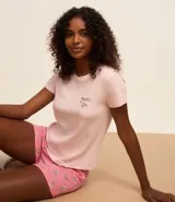 Conjunto de pijama short doll color rosa, compuesto por una remera de manga corta con estampado de texto y un short con estampado de flores.