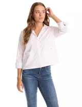 Camisa blanca de manga 3/4 con puños doblados, cuello en V y cierre de botones frontal. Presenta dos bolsillos delanteros con detalles de tachas metálicas.