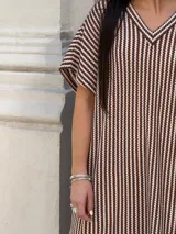 Vestido largo de tejido a rayas horizontales en tonos beige y blanco, con escote en V y mangas cortas tipo murciélago. Presenta tajos laterales en el ruedo.