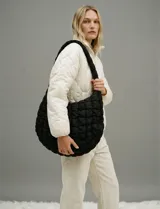 Bolso tipo hobo o baguette de color negro, con textura acolchada o capitoneada. Posee un asa ancha y gruesa del mismo material. El bolso tiene un forro interno a tono y bolsillos internos y externos ocultos.