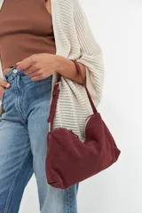 Cartera de hombro color bordó, confeccionada en gamuza, con correa ajustable y hebilla metálica.