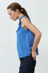 Top blanco sin mangas, con cuello alto y volados en los hombros. Presenta detalles de broderie en el cuello y el pecho, y cierre de botones en la parte superior delantera.