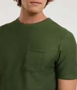 Remera de hombre color verde oliva, manga corta, cuello redondo y un bolsillo de parche en el pecho. La tela presenta una textura acanalada o de punto fino en relieve.