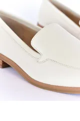 Mocasines de cuero color blanco hueso, con punta almendrada y suela marrón.