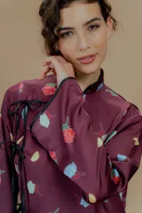 Vestido corto color borgoña con estampado de rosas y limones, mangas largas, cuello mao y cierre lateral con lazos negros.