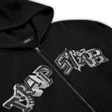 Conjunto deportivo negro de buzo con capucha y pantalón de jogging, ambos con logo "Trapstar" en letras góticas blancas con contorno plateado. El buzo tiene cierre frontal y bolsillo tipo canguro. El pantalón tiene cordón ajustable en la cintura y tobillos ajustables.