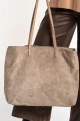Bolso tipo tote de gamuza vegana color camel, con asas de mano y logo grabado en el frente.