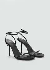 Sandalias negras de tacón fino, con tira delgada sobre los dedos y pulsera con hebilla al tobillo.