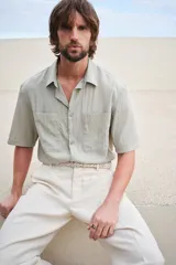 Camisa color verde claro con cuello inglés, tapeta lisa y canesú en la espalda. Modelo de manga corta con dos bolsillos superiores abiertos y bajo recto con aberturas laterales.