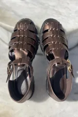 Sandalias de cuero color cobre con diseño de tiras entrecruzadas, hebilla lateral y suela track color negro.