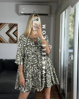 Vestido corto color verde oliva con estampado de hojas en blanco y negro, escote con lazo ajustable y mangas 3/4 acampanadas.