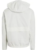 Campera blanca de poliéster con capucha y cierre frontal con cremallera. Tiene cuello alto, puños y ruedo elásticos, y un parche de goma con el logo de Calvin Klein en la manga izquierda.