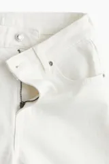 Pantalón jean blanco de corte ancho, tiro alto y largo tobillero. Confeccionado en denim de algodón levemente elástico, con cinco bolsillos, cierre frontal con botón y pierna amplia.