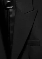 Blazer negro entallado con cuello de pico y solapa con muesca, manga larga, hombros estructurados, dos bolsillos de ribete delanteros, pinzas, abertura posterior y forro interior.