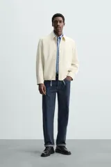 Sobrecamisa color crudo de corte regular fit, confeccionada en tejido con mezcla de viscosa. Tiene cuello solapa, manga larga con puños abotonados, bolsillo de parche en el pecho, bajo ajustable con cordones y cierre frontal con botones.