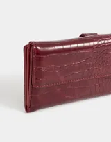 Billetera de cuerina color bordó con textura croco y lazo con broche con botón para cerrado.