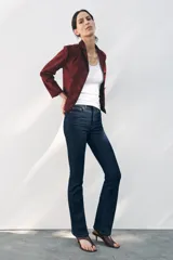 Pantalón de jean azul oscuro, de tiro medio, corte bootcut y largo hasta el tobillo. Tiene cinco bolsillos, trabillas en la cintura y cierre frontal con cremallera y botón metálico.